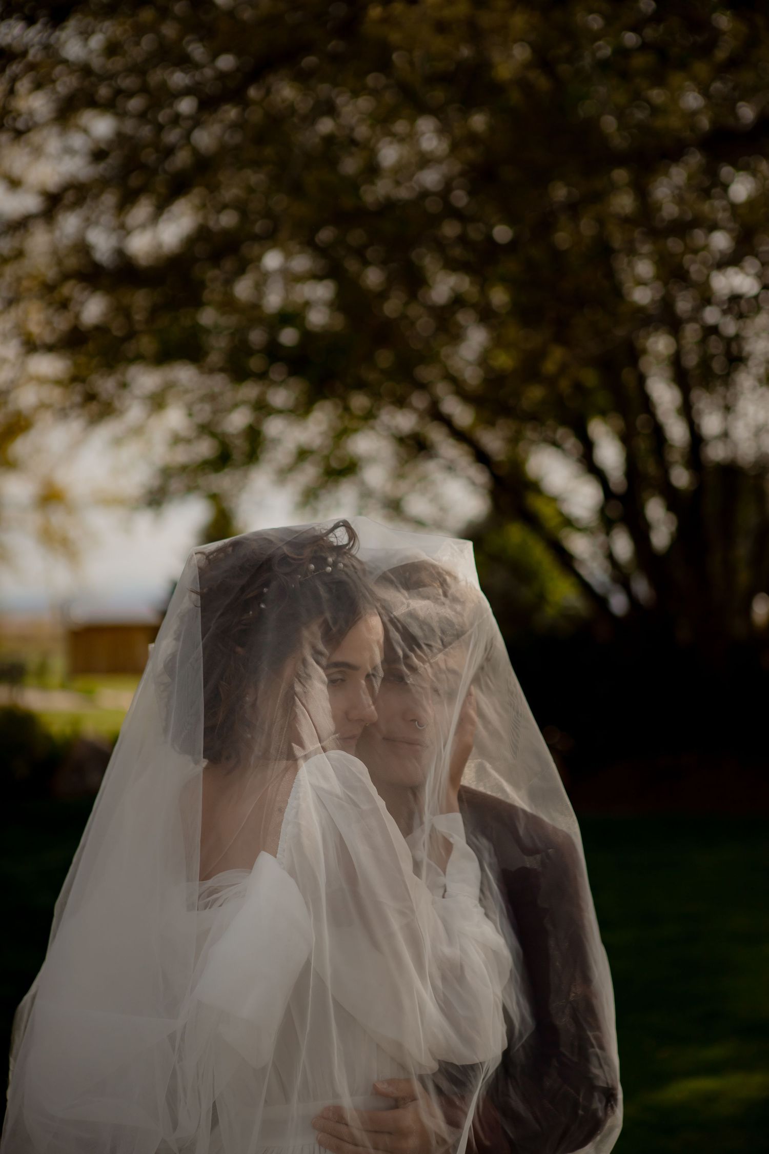 Newlyweds share an intimate moment beneath flowing white veil in garden setting.