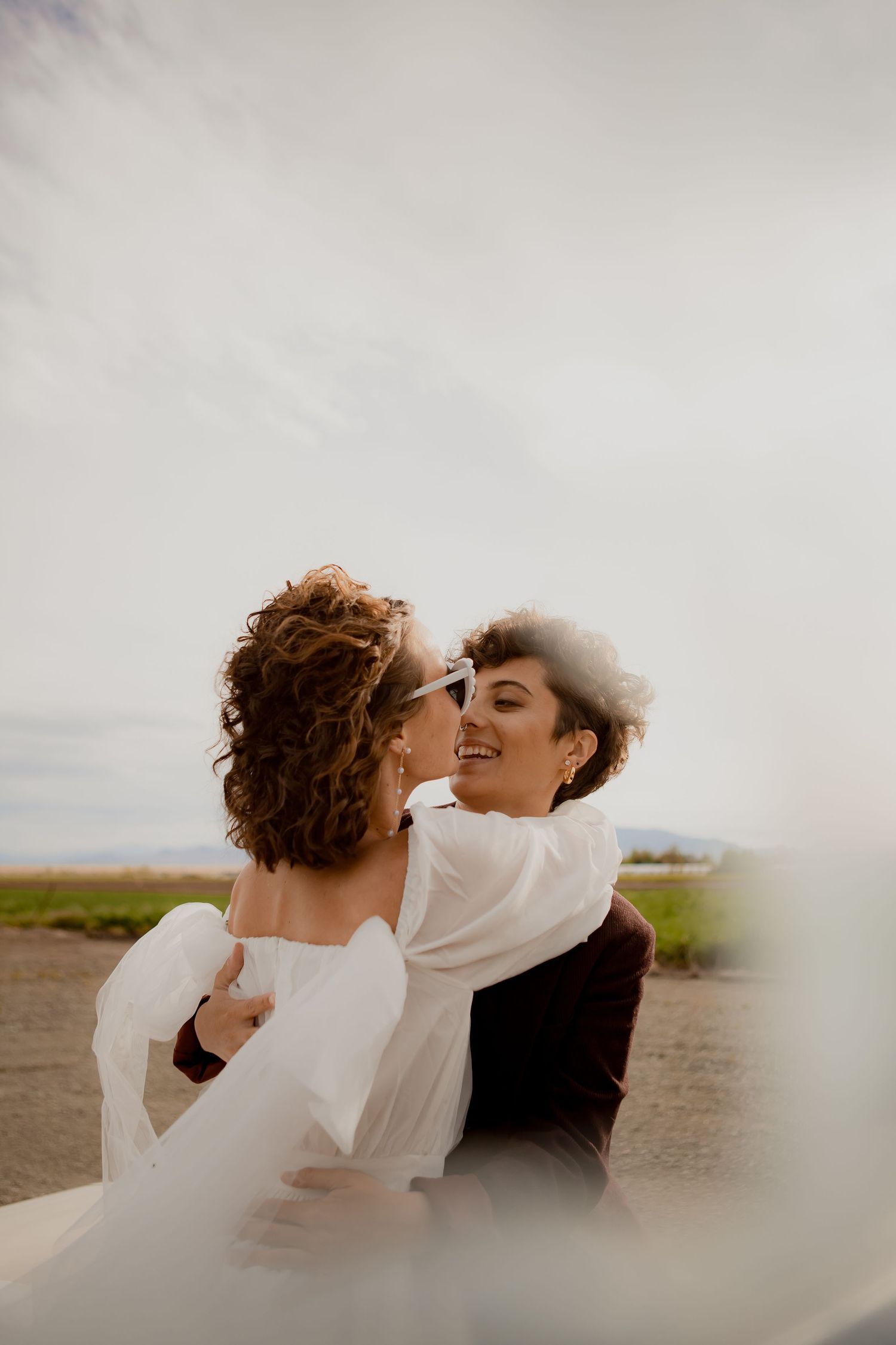 Couple sharing an intimate moment outdoors in white clothing against a cloudy sky.
