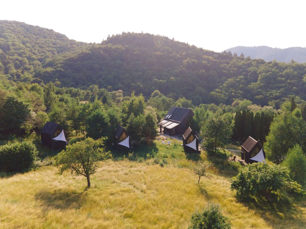Aerial view of wooden cabins scattered across a green mountainside meadow.