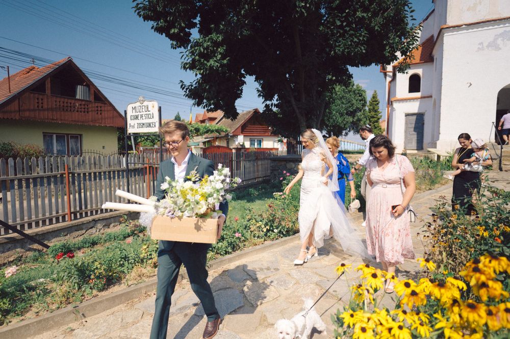 Group walking along garden path carrying flowers and decorations for celebration.