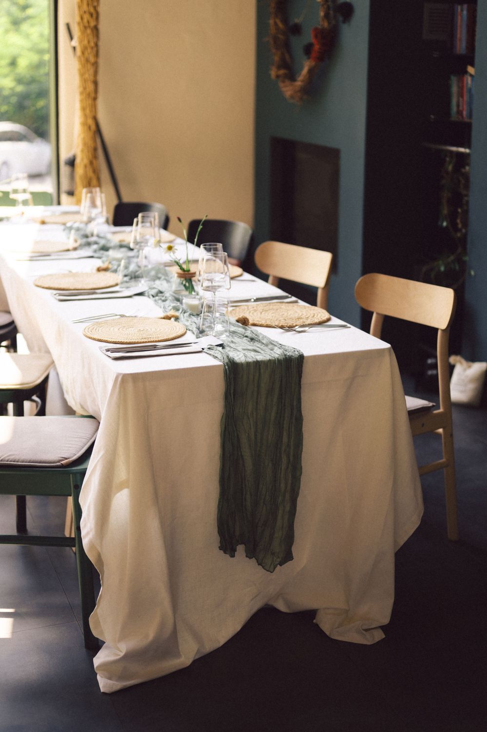 Elegant table setting with white tablecloth and dark green runner in dining room.