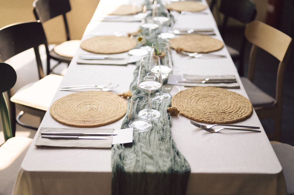Formal dining table set with woven placemats, white linens, and sage green table runner.