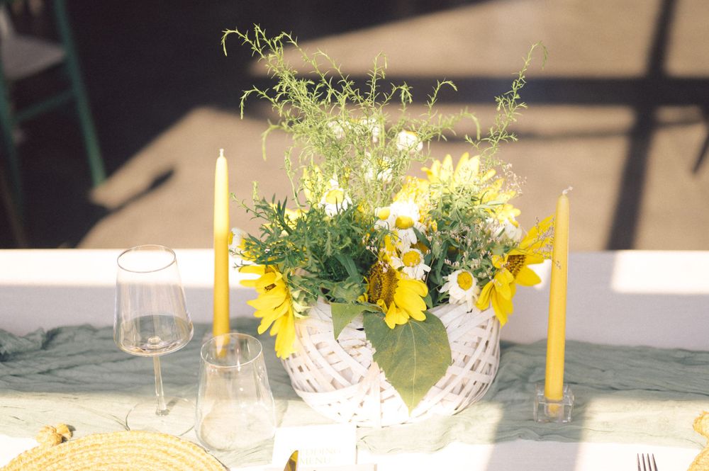 Yellow candles and floral centerpiece arrangement on white lace tablecloth for elegant table setting.