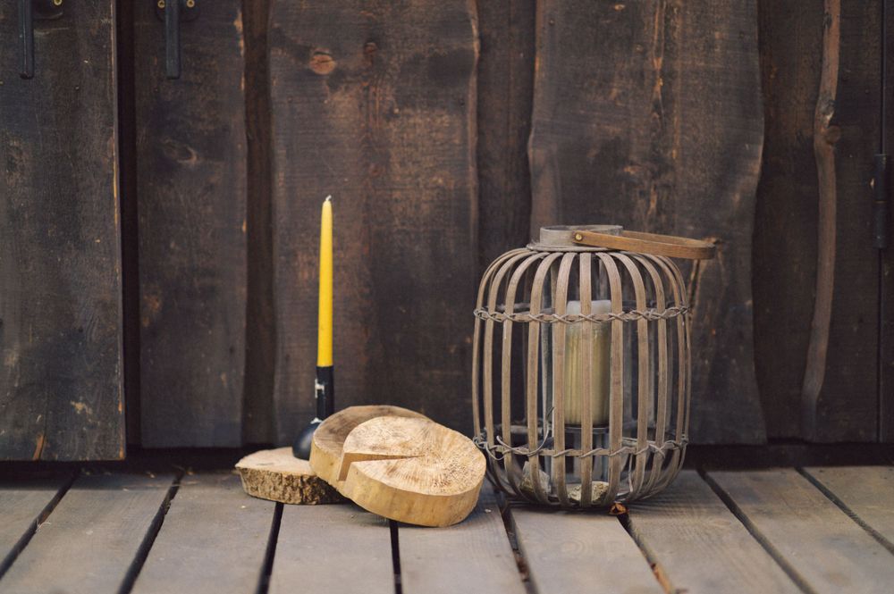 Rustic still life with yellow candle, bread, and vintage wire cage on wooden surface.