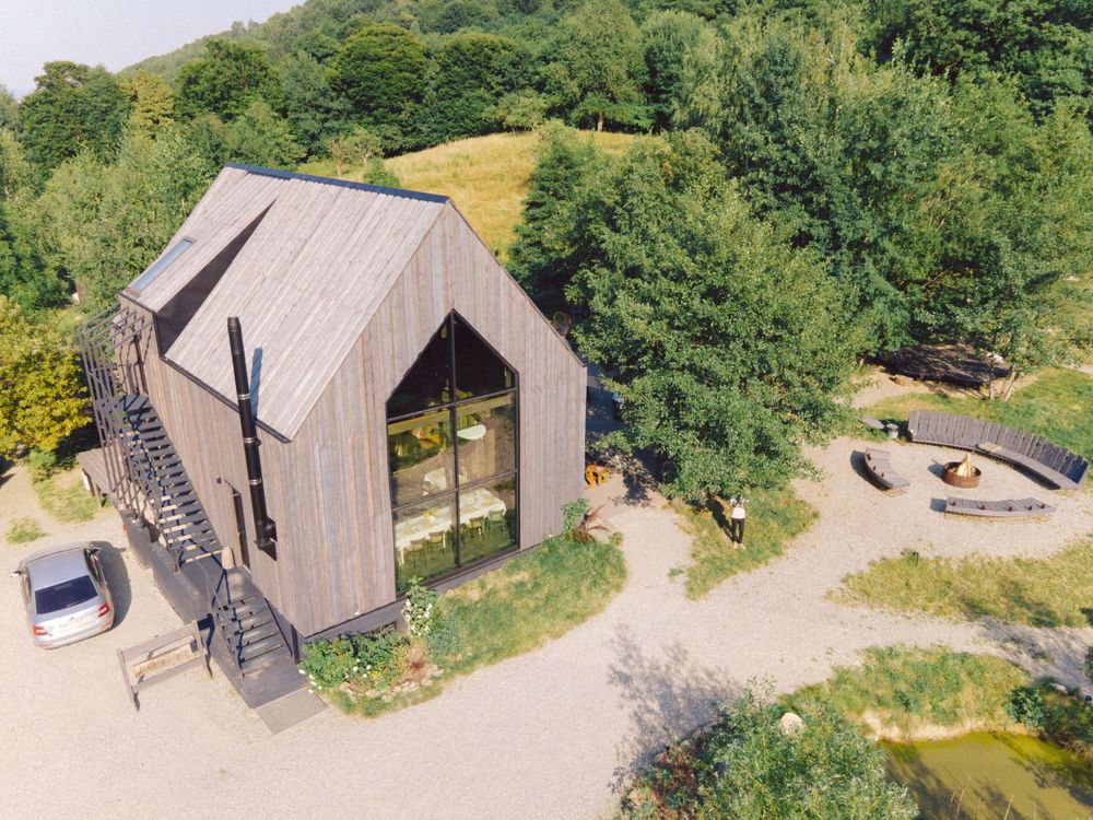 Modern architectural structure with steep roof and stairs surrounded by green landscape.