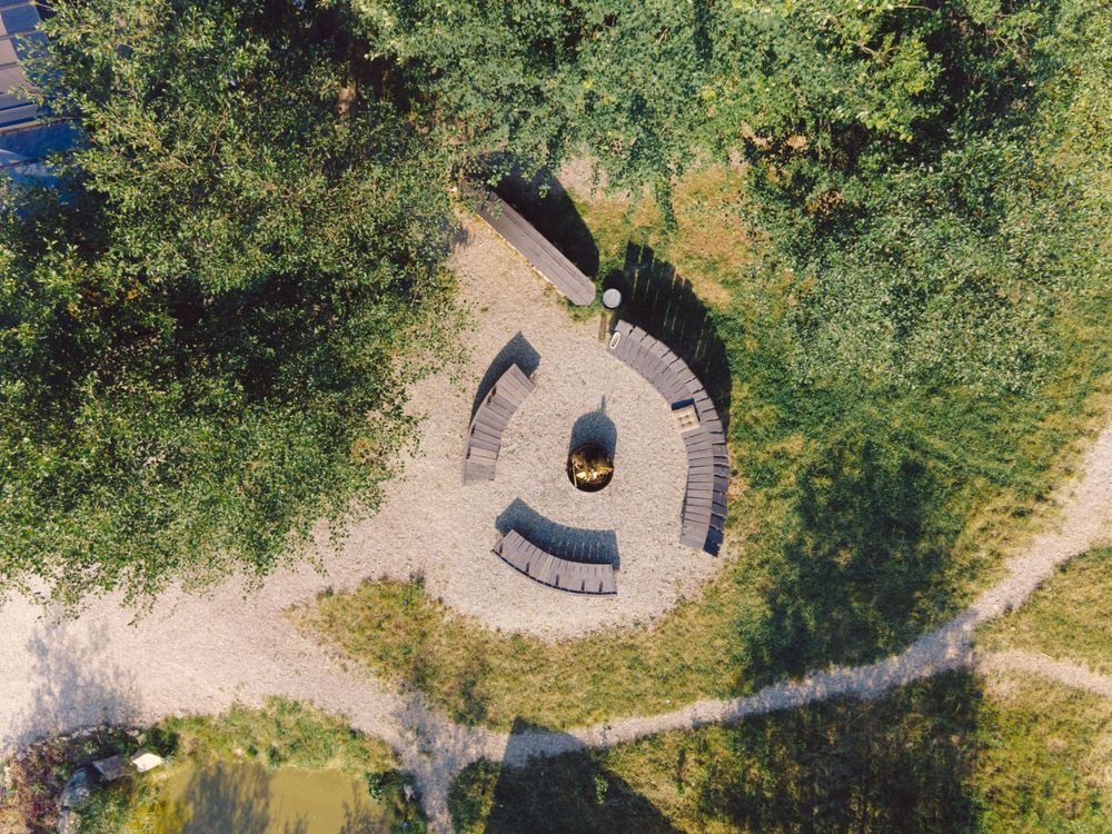 Circular stone seating area viewed from above surrounded by trees and pathways.