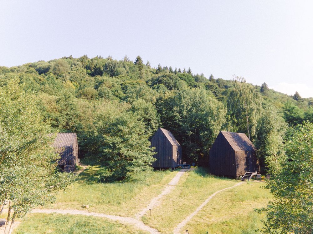 Three wooden cabin structures nestled among trees on hillside with connecting pathway.