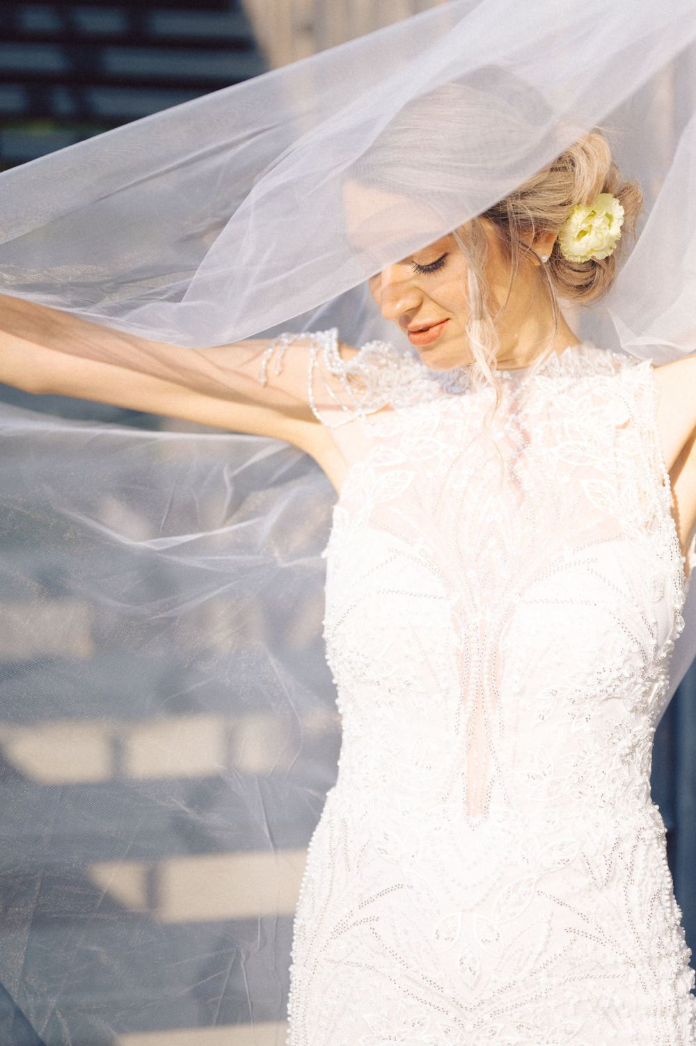 A delicate wedding veil flows in the breeze around an elegant white lace gown.