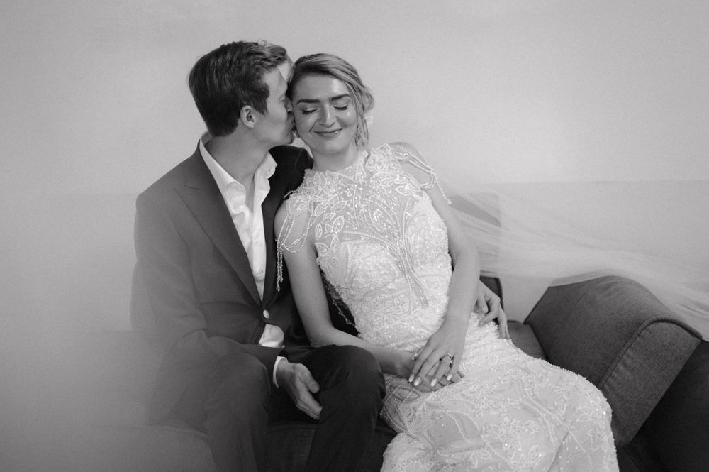 An intimate black and white portrait of newlyweds sharing a moment on a couch.