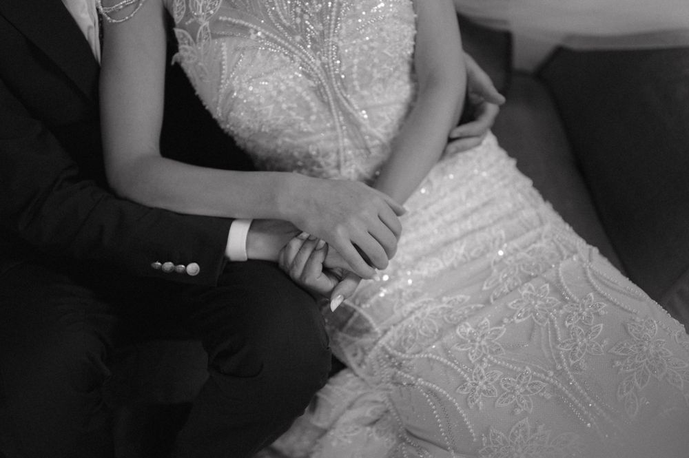 Black and white close-up of clasped hands and a lace wedding dress detail.