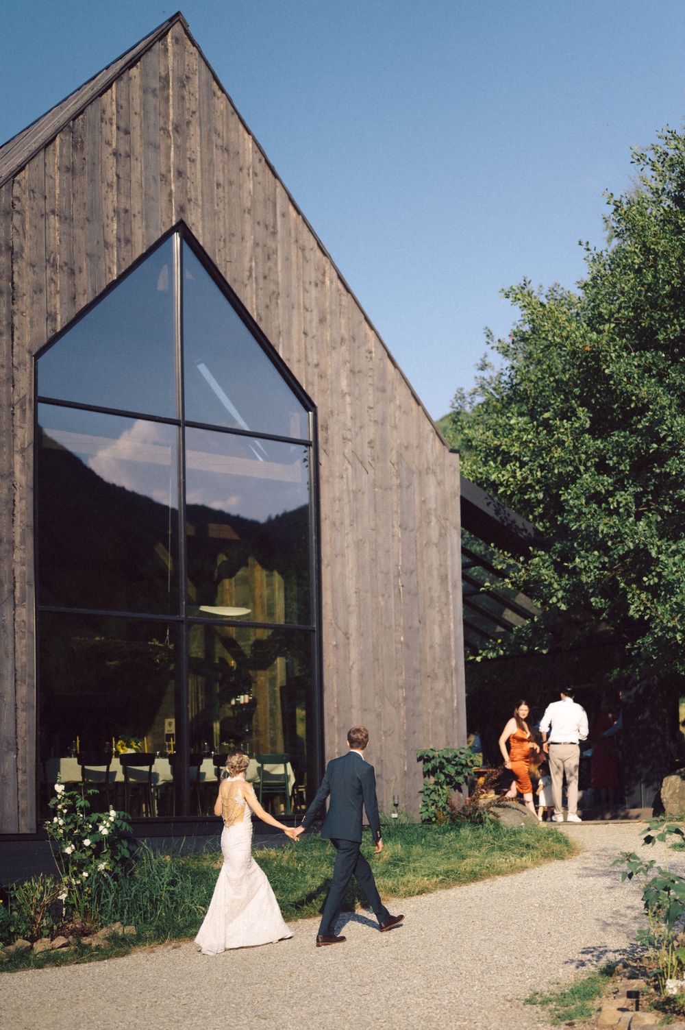 Modern wooden barn-style venue with large glass windows and couples walking outside.
