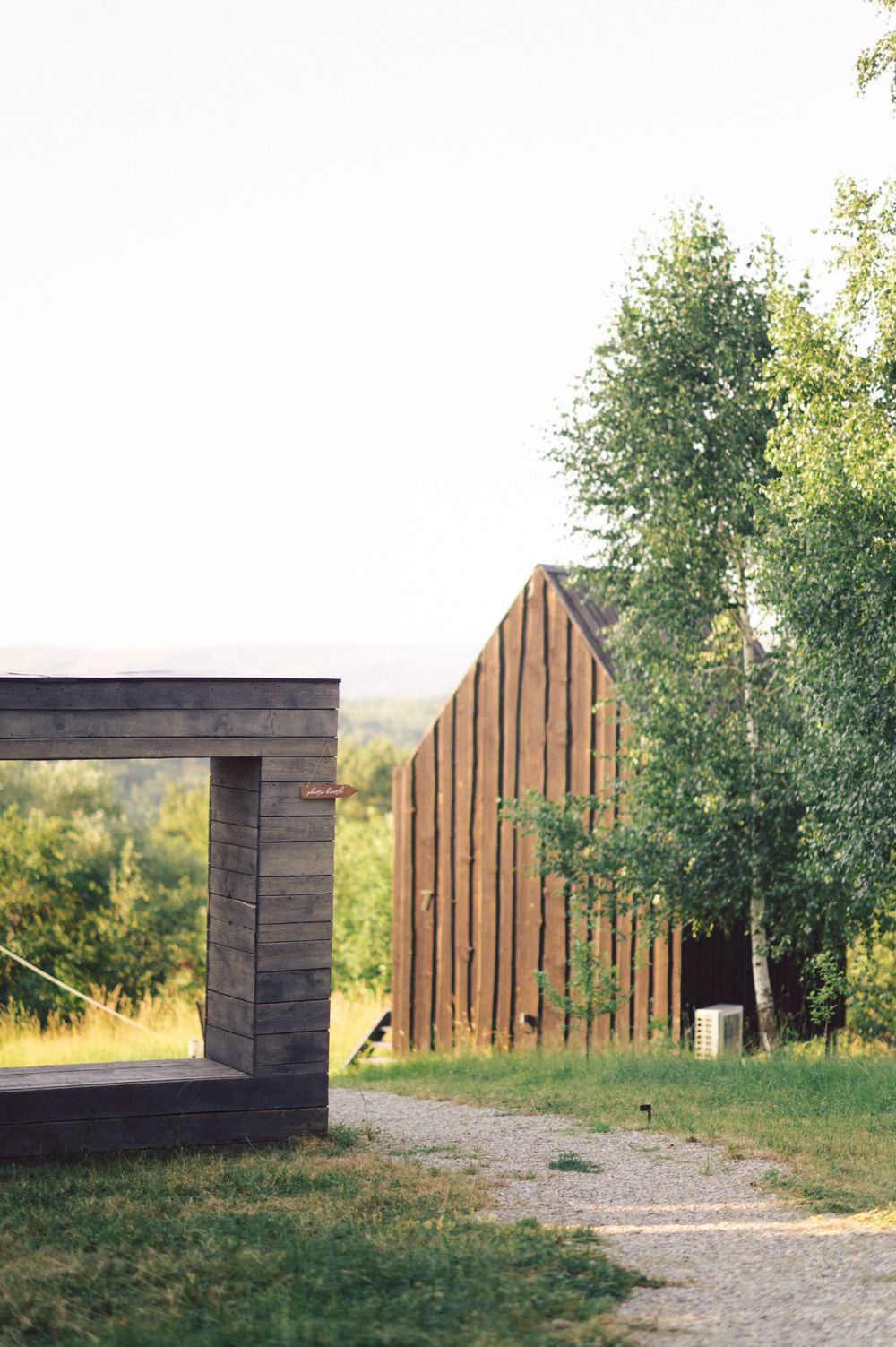 Rustic wooden buildings with steep angles connected by a gravel path surrounded by trees.