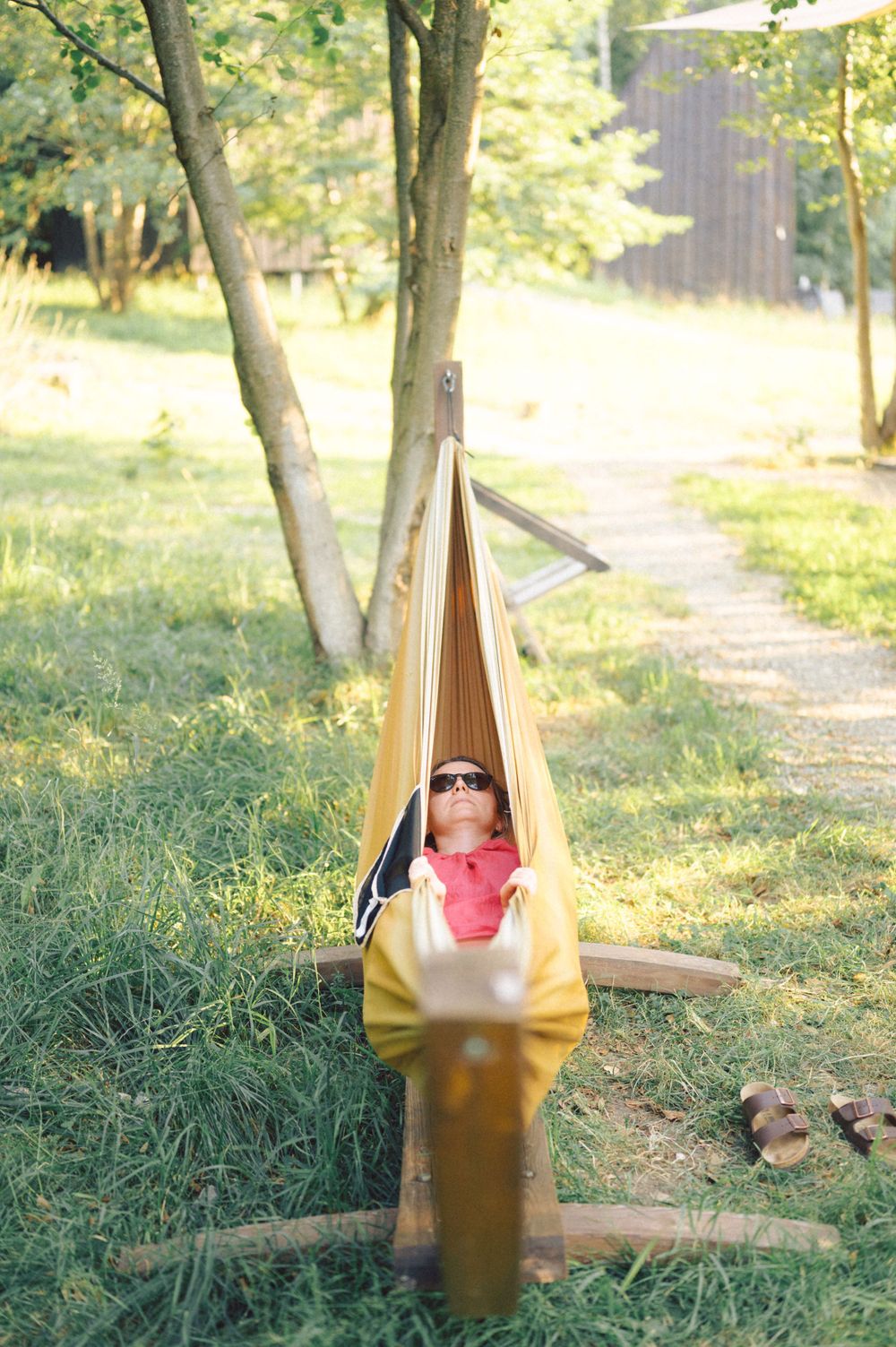 Person relaxing in yellow hammock with drink during outdoor gathering.