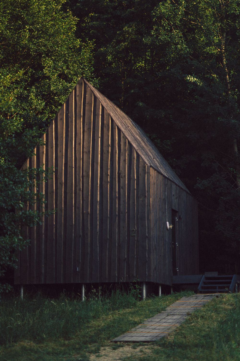 Angular wooden structure with vertical planks nestled among trees at dusk.
