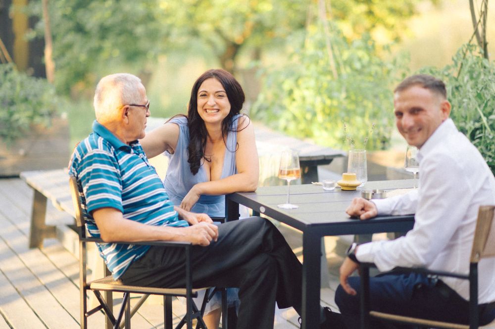 Three people enjoying casual conversation over drinks on an outdoor patio.