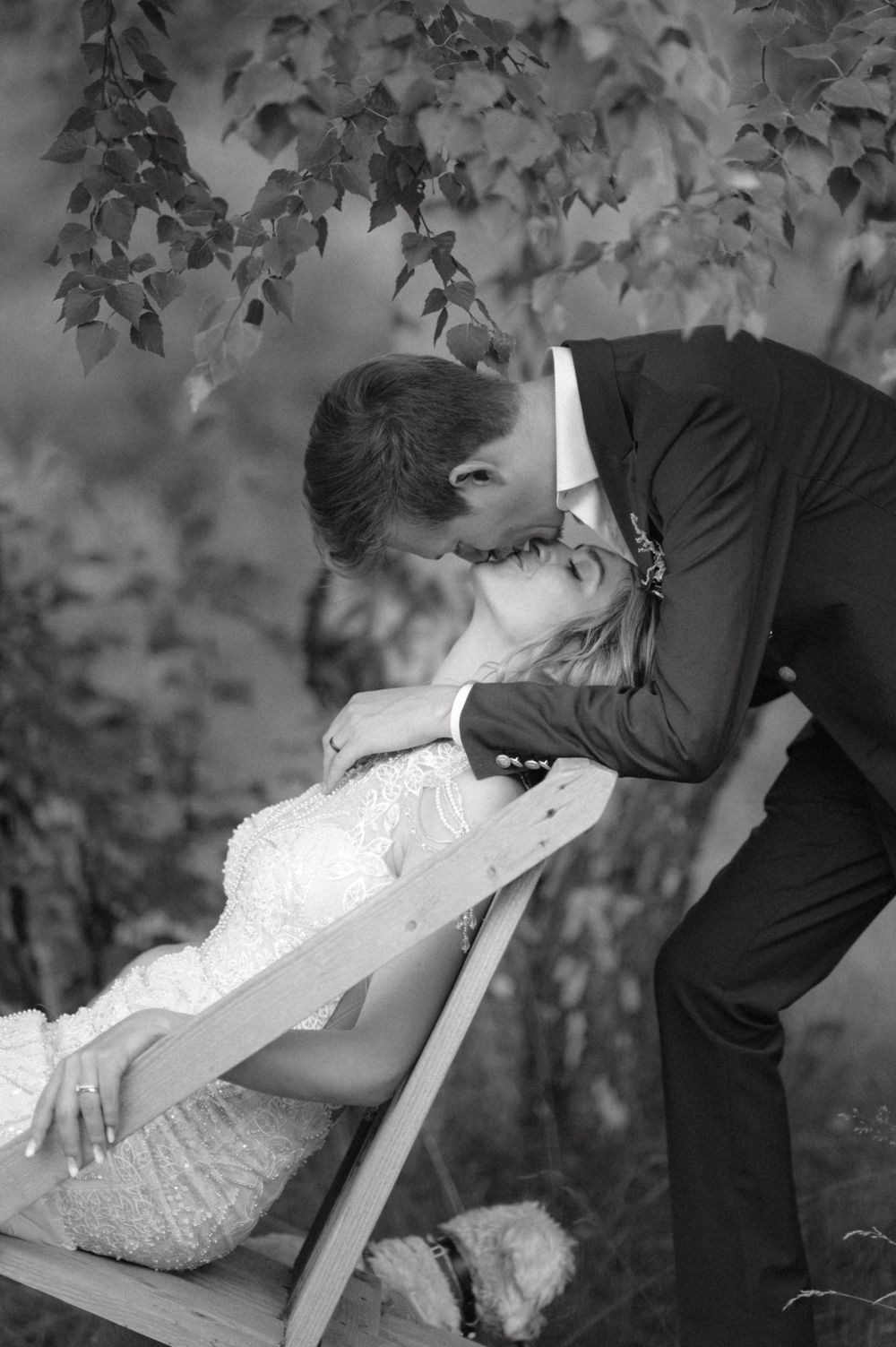 Romantic black and white wedding photo of couple sharing an intimate moment near foliage.