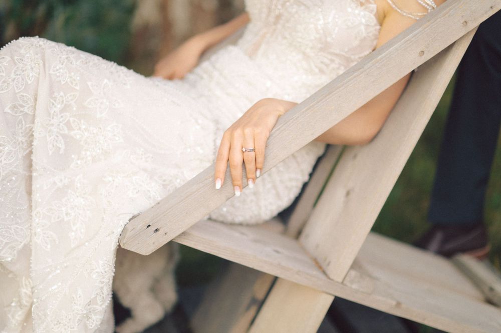 Close-up detail shot of bride's hand with ring while sitting on white wooden bench.