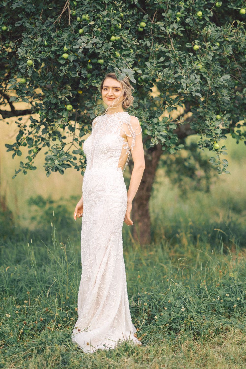 Elegant bride in fitted lace wedding dress poses under tree branches.