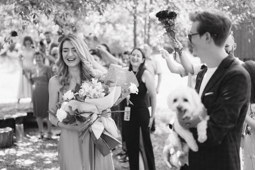 Black and white photo of celebration with guests throwing confetti at outdoor ceremony.