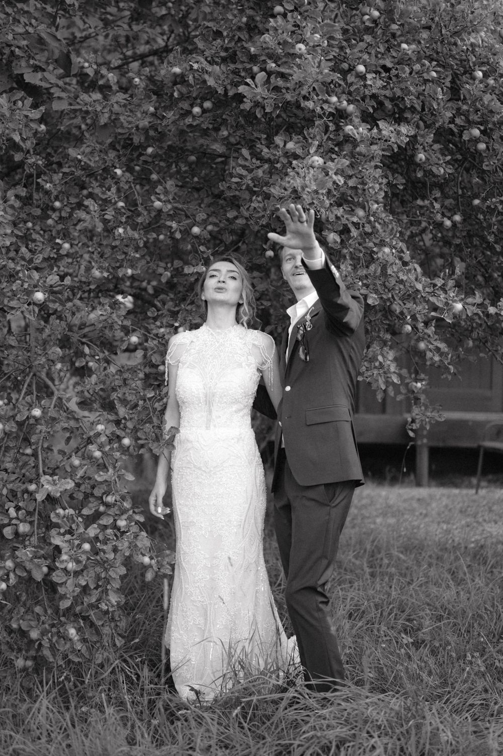 Black and white photo of couple reaching up to touch tree leaves.