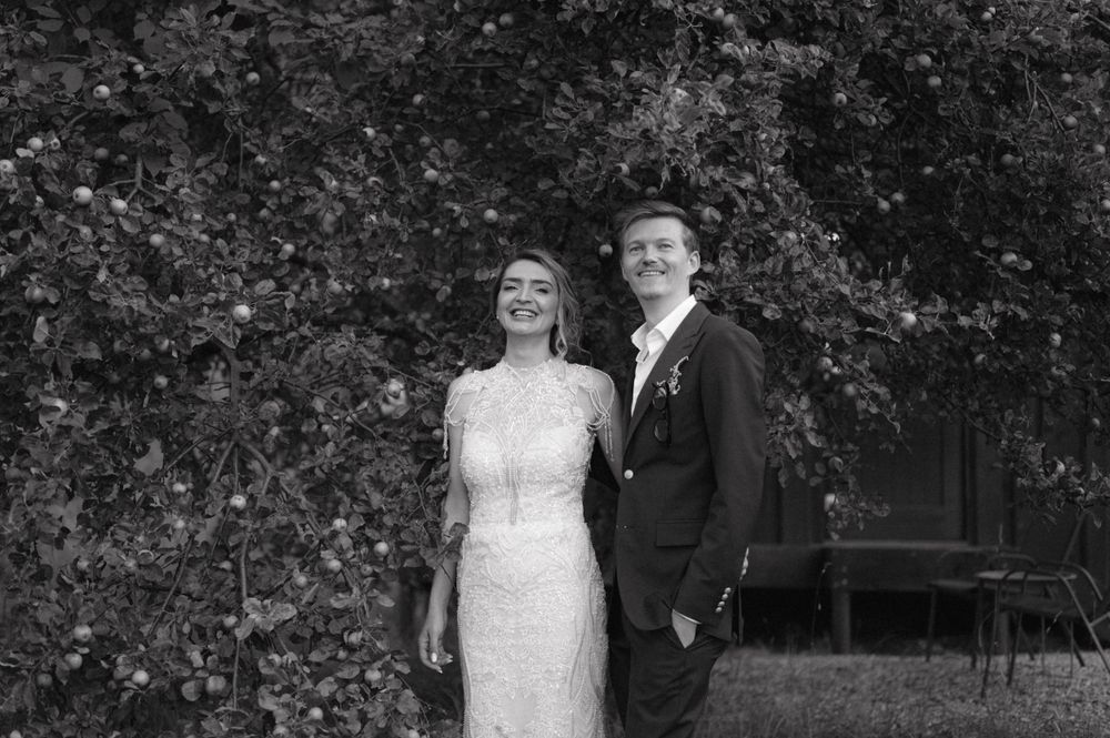 Black and white portrait of couple smiling under garden foliage.