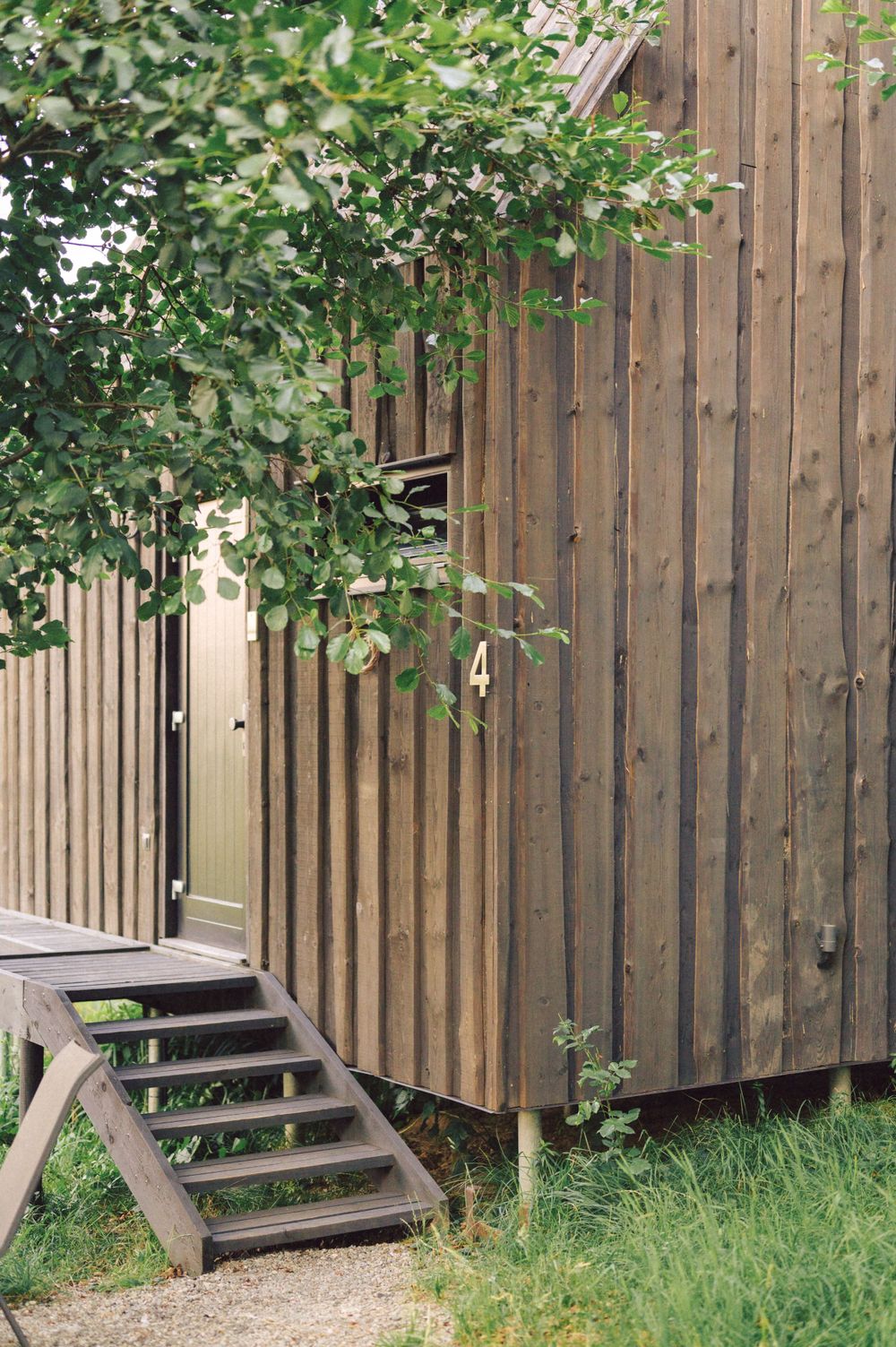 Wooden cabin exterior with vertical slats and small staircase surrounded by green foliage.