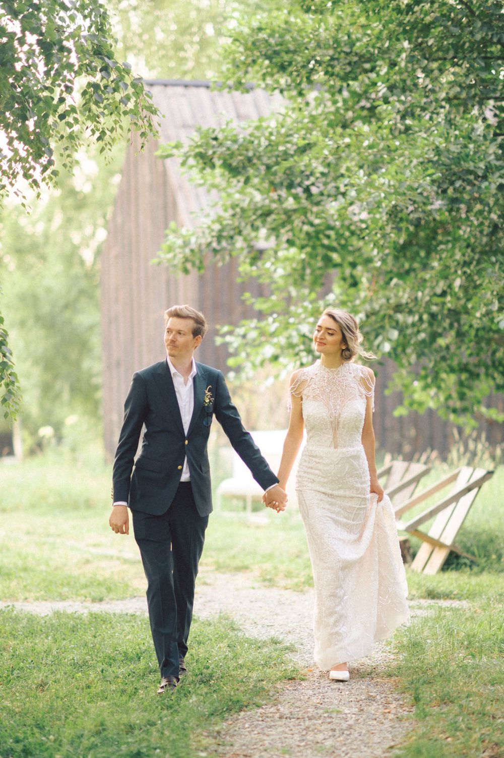 A couple walks hand in hand along a garden path on their wedding day.