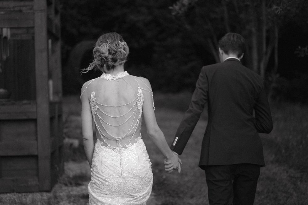 Back view of a couple walking together, showing detailed lace back of wedding dress.