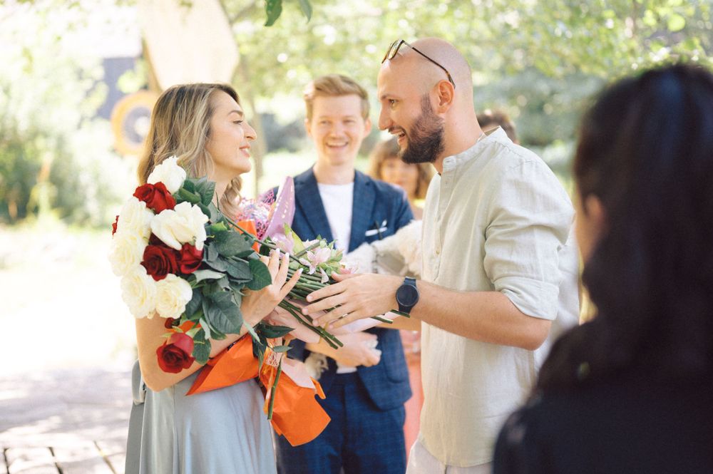 Guests present flowers during outdoor celebration with natural sunlit backdrop.