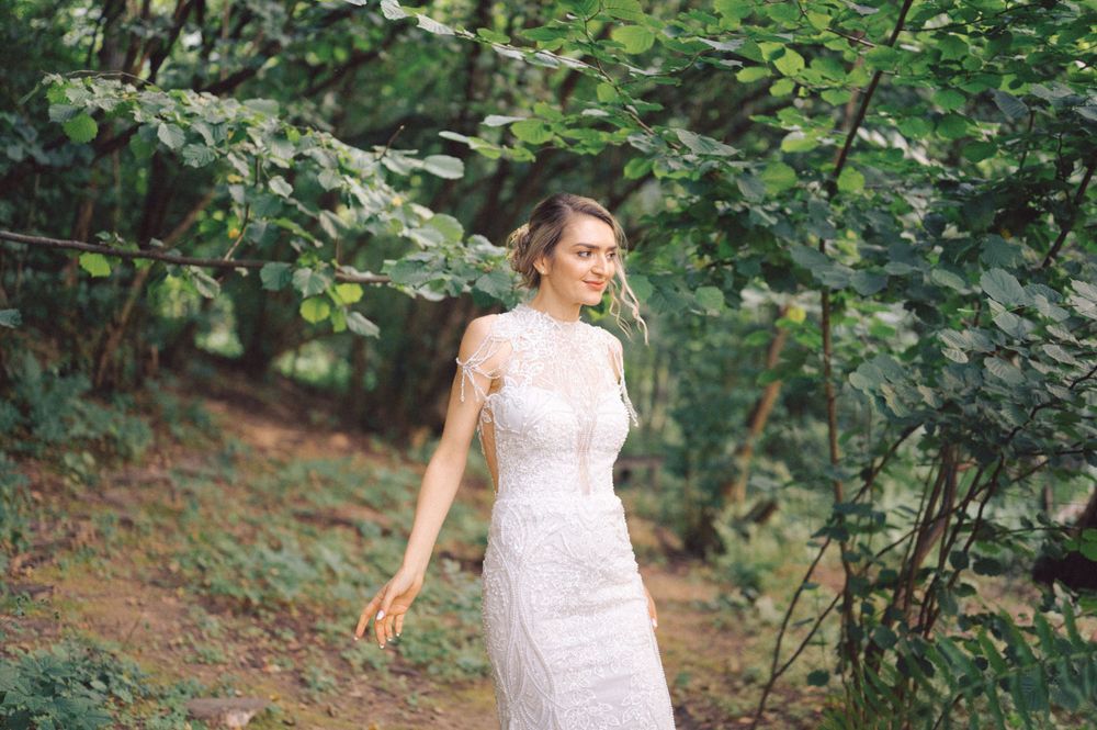 A person in a fitted white lace dress walks through a lush green forest setting.