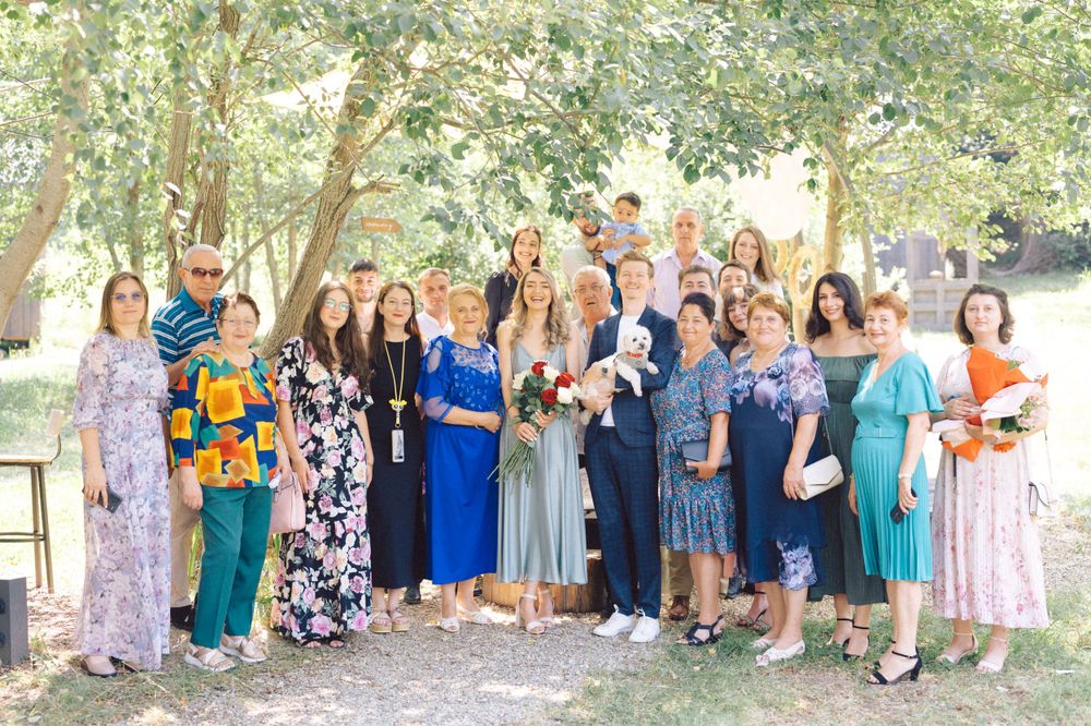 A large group in colorful dresses poses together outdoors for a wedding party photo.