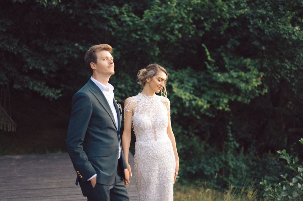 A couple in wedding attire standing together on a path surrounded by green foliage.