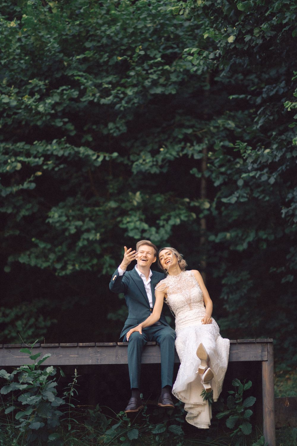 A couple sharing a playful moment while sitting on a wooden bench in a forest setting.