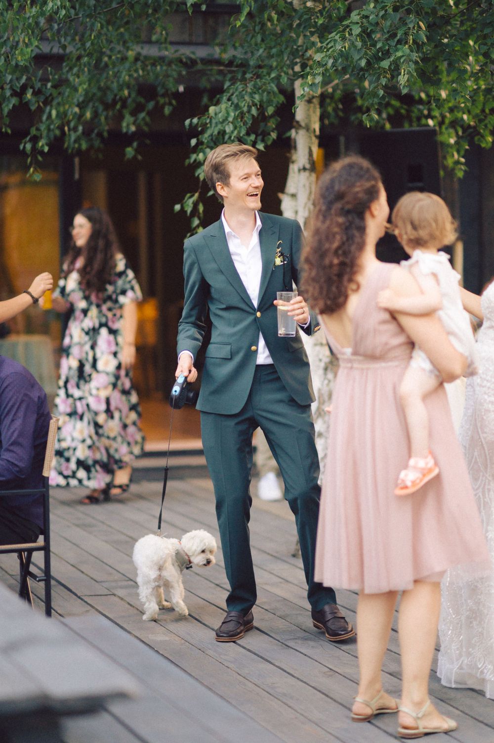 Guests socializing on a wooden deck during an outdoor event with a small white dog present.