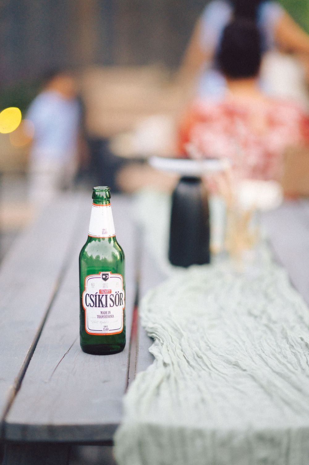 A bottle of Csiki Sor beer sits on a wooden table with a cloth runner.