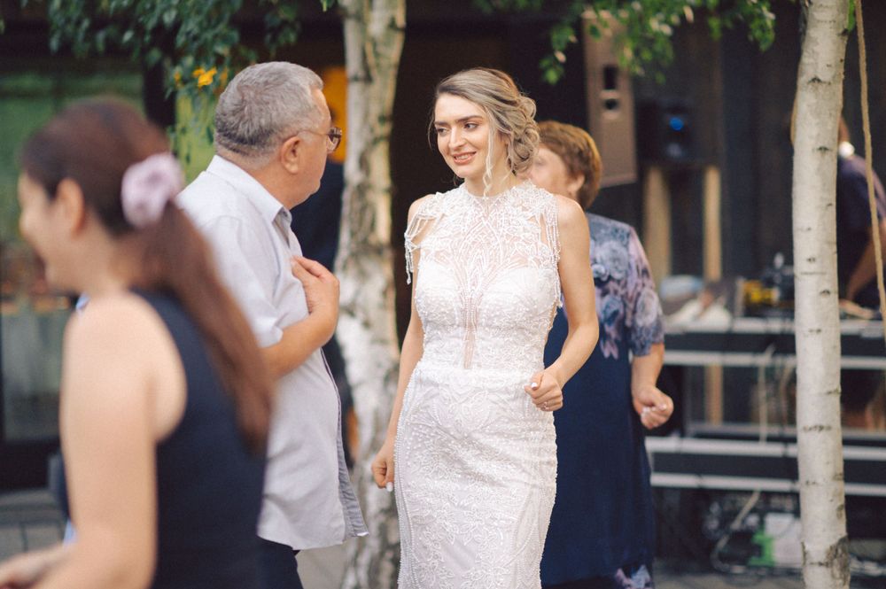 Elegant white lace wedding dress being shown at an outdoor venue with guests in the background.