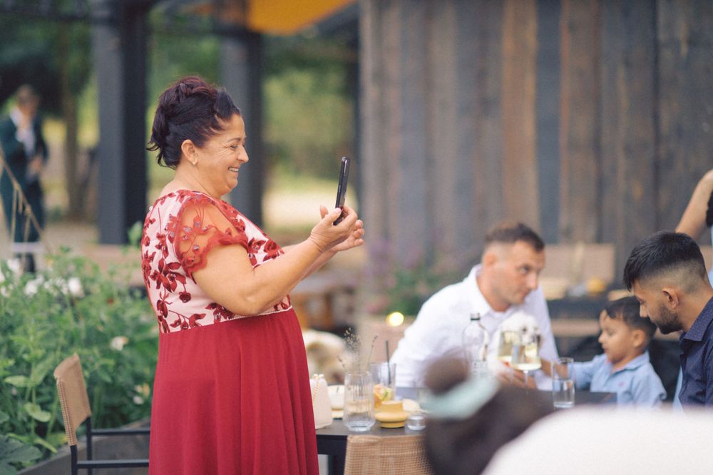 Woman in red floral dress taking photos at an outdoor gathering.
