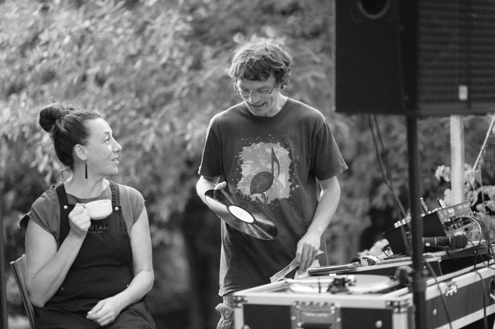 Two people chatting while working with DJ equipment at an outdoor event.