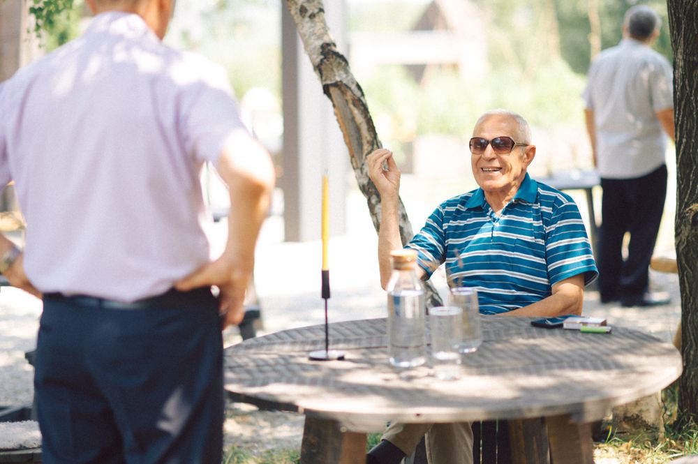 Casual outdoor conversation at a round table in a sunny garden setting.