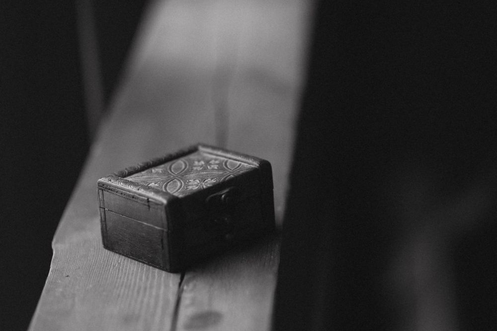 A black and white close-up of a small ring box on a wooden surface.
