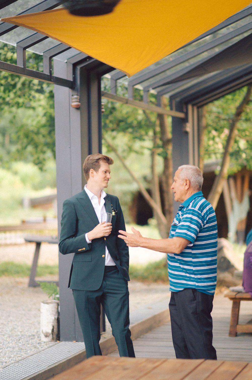 Two people having a conversation under a yellow awning at an outdoor venue.