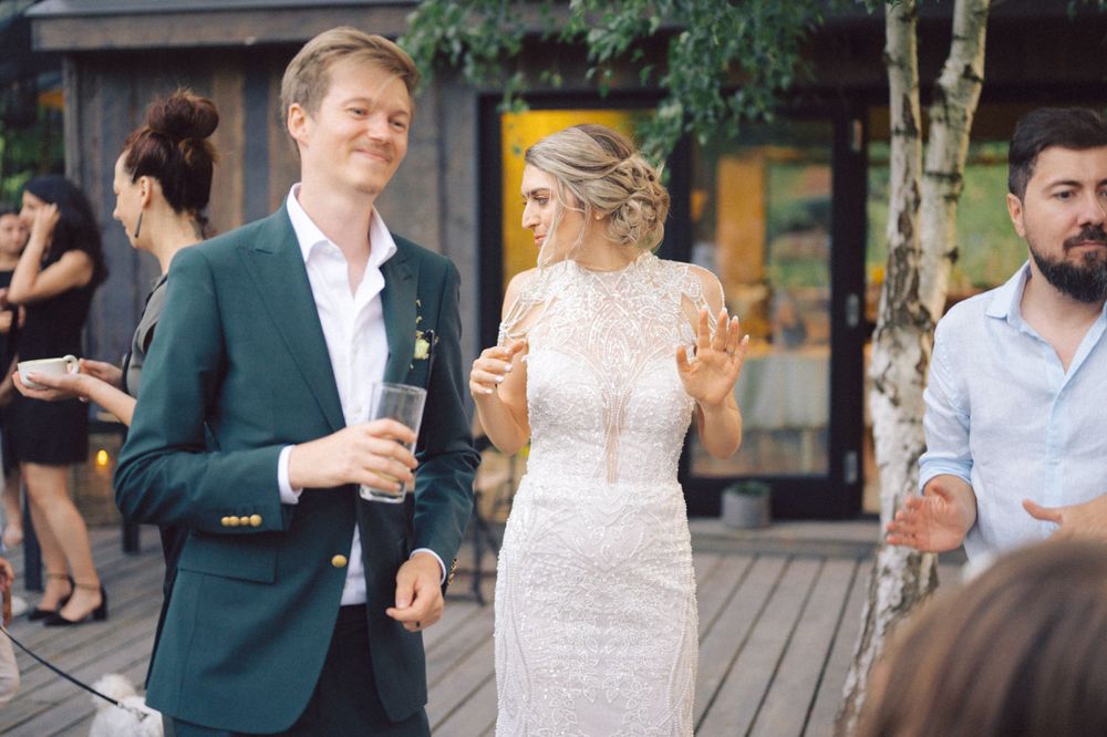 Wedding guests mingling on wooden deck at outdoor venue.