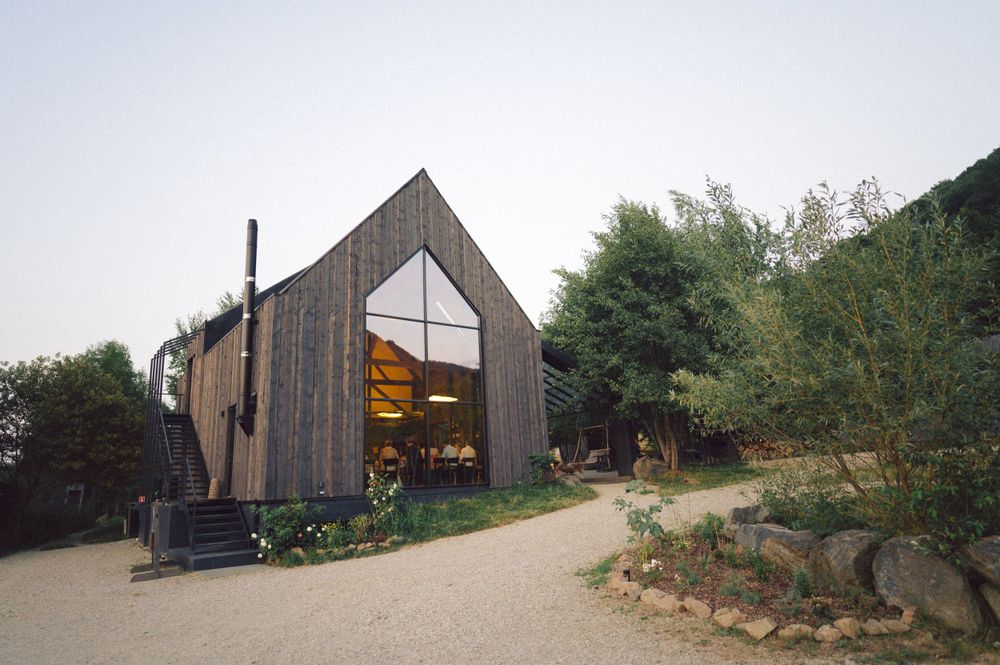 Modern wooden barn-style building with glass features and outdoor garden area.