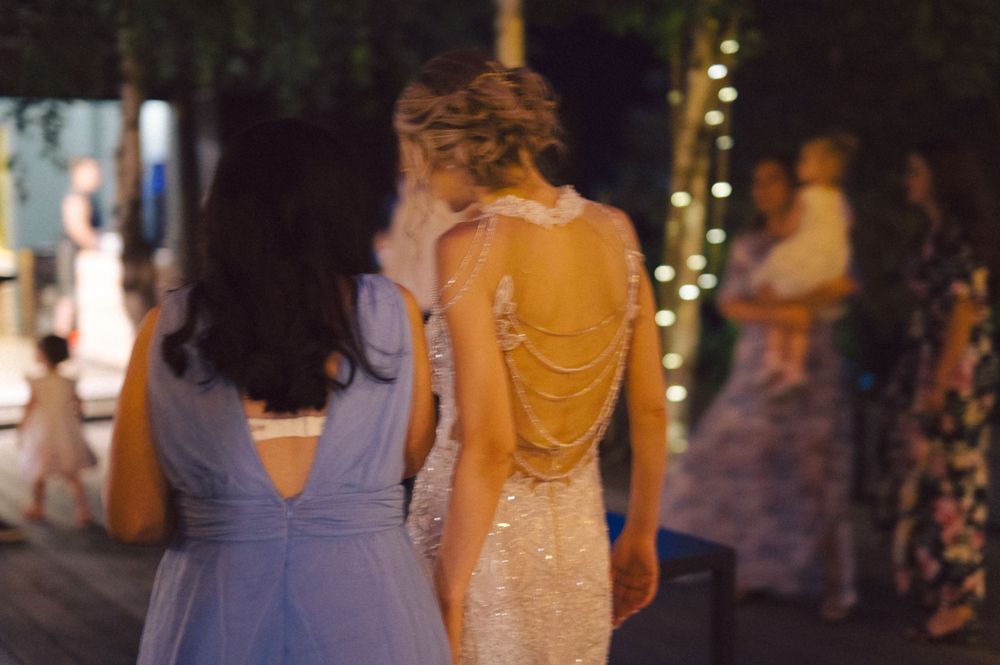 Two party guests in formal attire at an evening outdoor celebration with string lights.