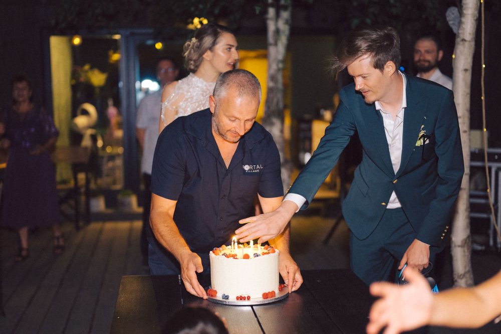 Evening celebration scene with a lit birthday cake being presented at an outdoor venue.