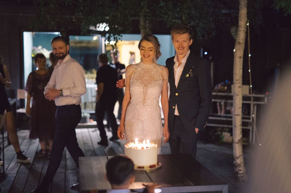 Couple standing by a glowing cake at an outdoor evening celebration.