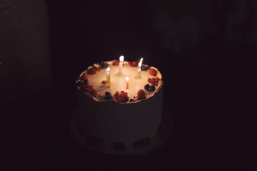Close-up of a white cake with multiple lit candles glowing in darkness.