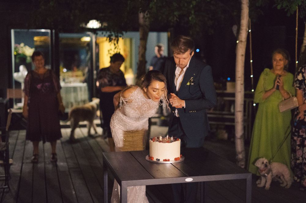 Couple leaning over to blow out candles on a birthday cake at an outdoor evening celebration.