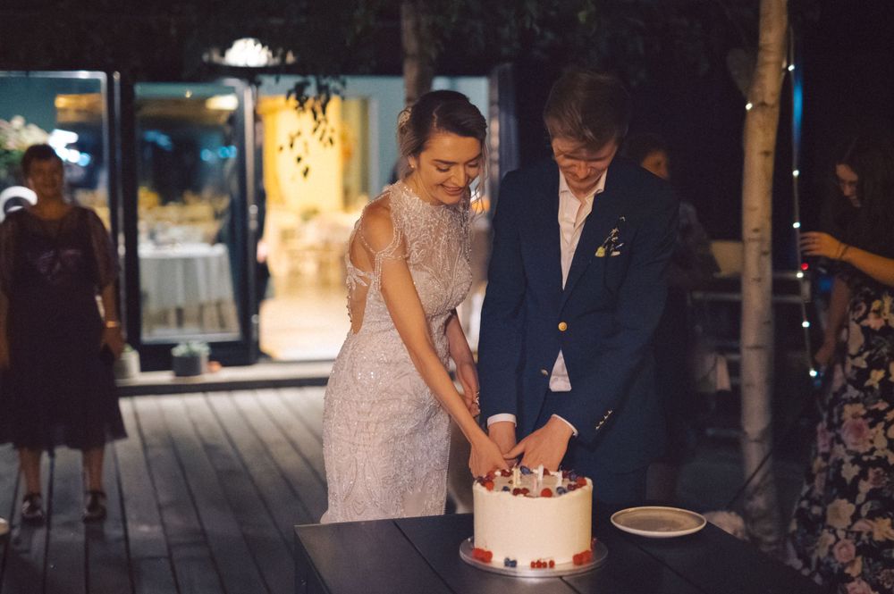 A couple cutting their white wedding cake together during an evening outdoor reception.
