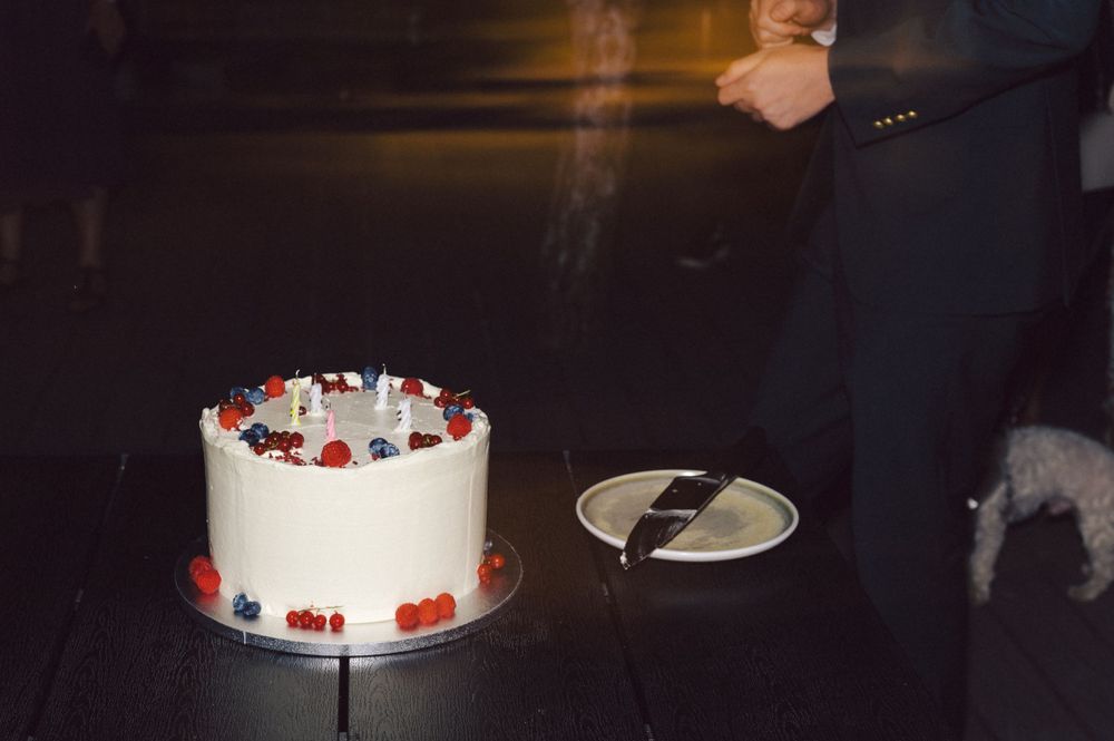 A white wedding cake decorated with fresh berries on a dark table.